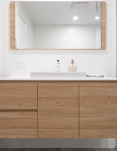 Timber bathroom cabinetry with square white basin and mirror above.