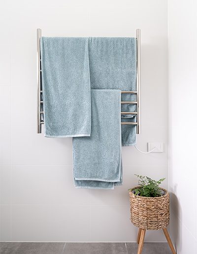 New bathroom heated towel rack against white wall.