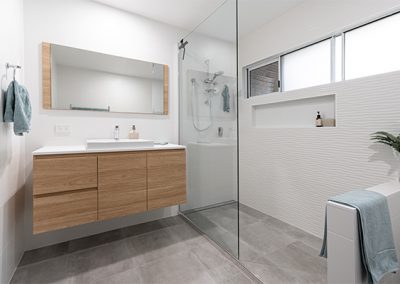 New bathroom with wavy white shower tile feature, timber cabinetry and stone-look flooring.