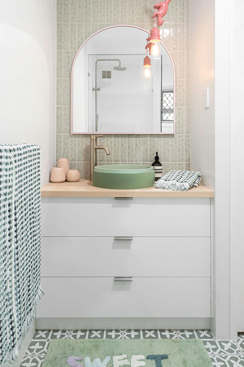 White bathroom with vertical tiles, a matt white sink and timber vanity with a large round mirror on the wall